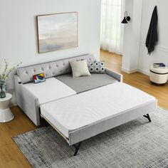 a couch bed sitting on top of a wooden floor next to a white rug and window