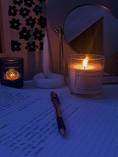 a lit candle sitting on top of a desk next to a pen and paper with writing