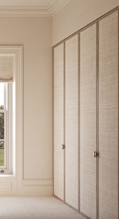 an empty room with white walls and beige closets next to a window that looks out onto a grassy field