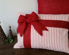 a red and white striped pillow with a bow on the side next to two small christmas trees