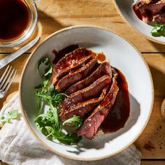 a white bowl filled with meat and greens on top of a wooden table next to a cup of tea