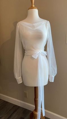 a mannequin wearing a white shirt with sheer sleeves and a bow tie around the waist