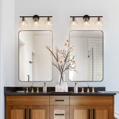 a bathroom vanity with two mirrors above it and flowers in vase on the counter top