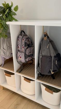 a white shelf filled with lots of backpacks and baskets next to a potted plant