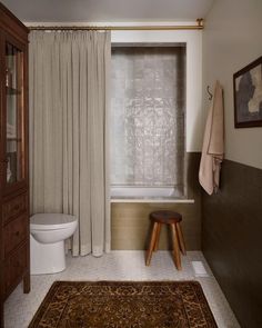 a bath room with a toilet a rug and a shower curtain next to a tub