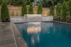 a pool surrounded by trees and shrubbery next to a wall with water running down it