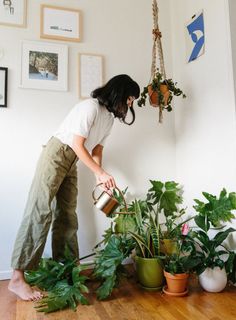 a woman watering plants on the floor in front of some pictures and hanging planters