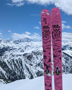 a pair of pink skis sitting on top of a snow covered slope with mountains in the background