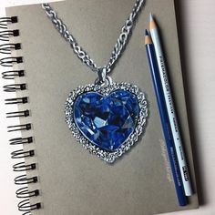 a drawing of a heart shaped necklace with a blue crystal in the center and a pencil next to it