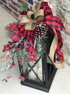 a christmas lantern decorated with pine cones, berries and burlocks is sitting next to a brick wall