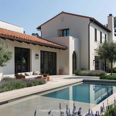 a house with a pool in front of it and purple flowers growing around the pool