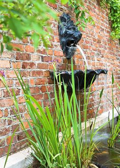 a water fountain in front of a brick wall with green plants growing on the sides