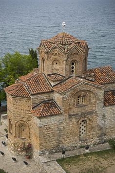 an old church with red tile roof next to the ocean