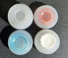 four white bowls with different colored lids sitting on top of a gray tablecloth covered floor