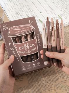 a person holding a box of coffee pencils in front of a stack of pens