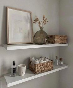 two white shelves with baskets and towels on them in a bathroom area next to a framed photograph