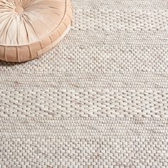 a white rug on the floor next to a wooden stool with a round seat cushion