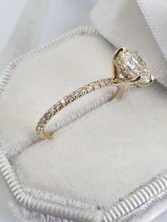 a diamond engagement ring sitting on top of a white cloth covered box with its lid open