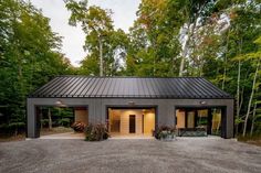 a garage with two doors and windows in the middle of a gravel lot surrounded by trees