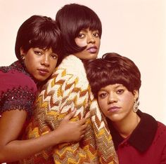 three women are hugging each other in front of a white background and one is wearing a red sweater