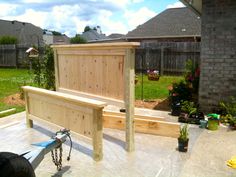 a wooden bed frame sitting on top of a cement floor next to a garden area