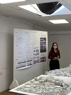 a woman wearing a face mask stands in front of a model of a city with buildings on it