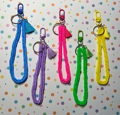 four different colored keychains with tassels on them sitting on a polka dot background