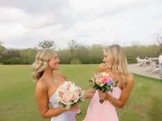 two beautiful women standing next to each other on a lush green field holding bouquets