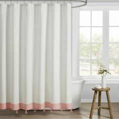 a white bath tub sitting next to a window with pink trim on the shower curtain