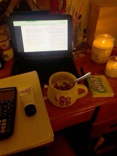 a laptop computer sitting on top of a desk next to a cup of cereal and a calculator