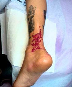 a person with a tattoo on their foot has a red flower in the shape of a dragon