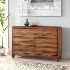 a wooden dresser sitting in front of a window next to a painting on the wall