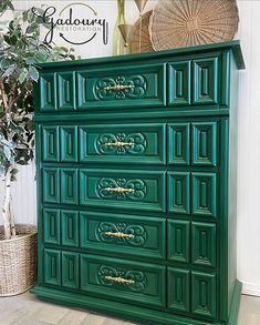 a green dresser with gold handles in a room next to a potted plant and wicker basket