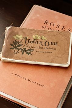 two old books sitting on top of a wooden table next to each other, one has a flower guide