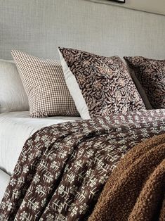 a neatly made bed with brown and white pillows on top of it's headboard