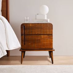 a nightstand with a lamp on top of it next to a white rug and bed