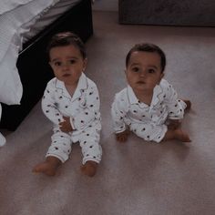 two babies sitting on the floor next to each other wearing pajamas and looking at the camera