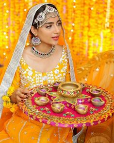 a woman in an orange and yellow outfit holding a tray with gold dishes on it