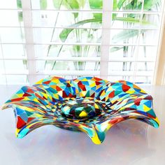 a colorful glass bowl sitting on top of a white table next to a planter