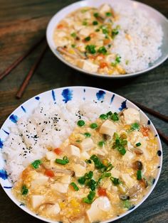 two plates filled with rice and chicken on top of a wooden table next to chopsticks