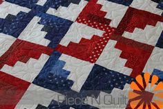 a red, white and blue quilt is displayed on a table top with an orange flower in the center