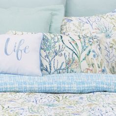 a bed with blue and white sheets, pillows and a pillow that says life on it