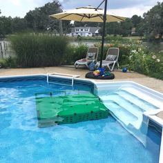 an empty swimming pool with two lawn chairs and umbrellas in the back yard area