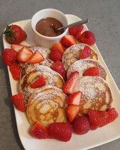 some pancakes and strawberries on a white plate with chocolate dipping in the middle for toppings