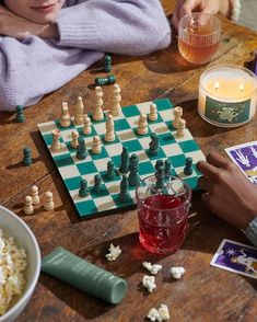 two people sitting at a table playing chess and drinking wine with popcorn on the side