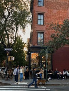 people are walking across the street in front of a brick building with an awning