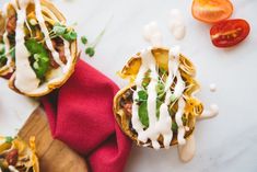 some taco shells are sitting on a cutting board with tomatoes and other food items