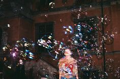 a woman standing in front of a building with lots of soap bubbles floating around her