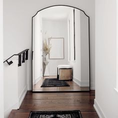 an arched mirror in a white room with wood flooring and black trim on the wall