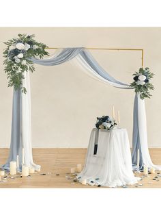 a white and blue wedding arch decorated with greenery, candles and flowers on a wooden floor